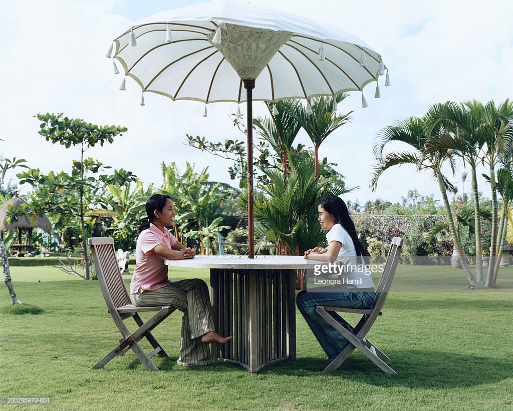 two young women sitting table under umbrella side view stock ture outdoor adjustable drum throne round concrete teal bedroom chair small metal accent couch plans moroccan lamp